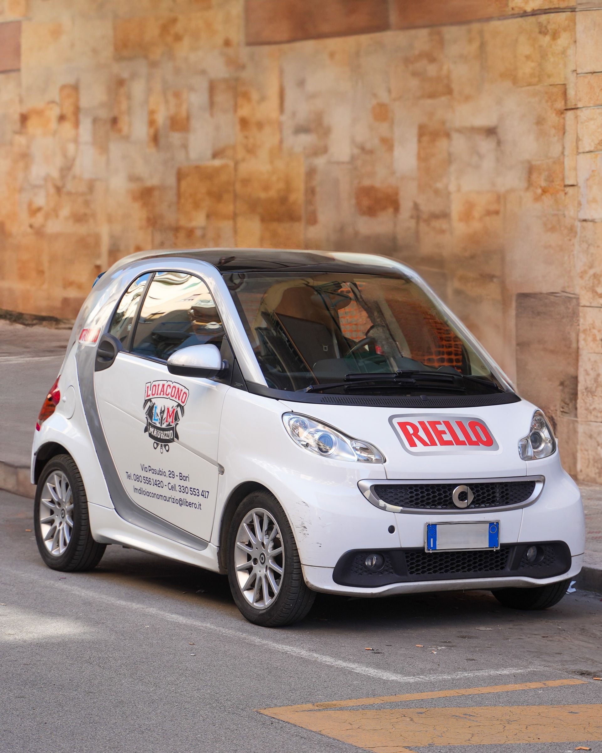 Smart bianca parcheggiata su una strada cittadina; ha la scritta