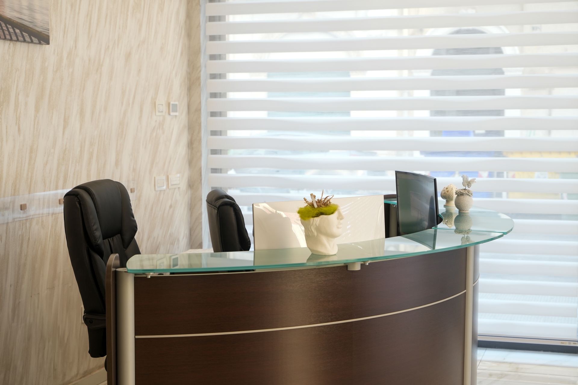 Bancone della reception con piano in vetro, sedia nera e tende a strati in un moderno ambiente d'ufficio.