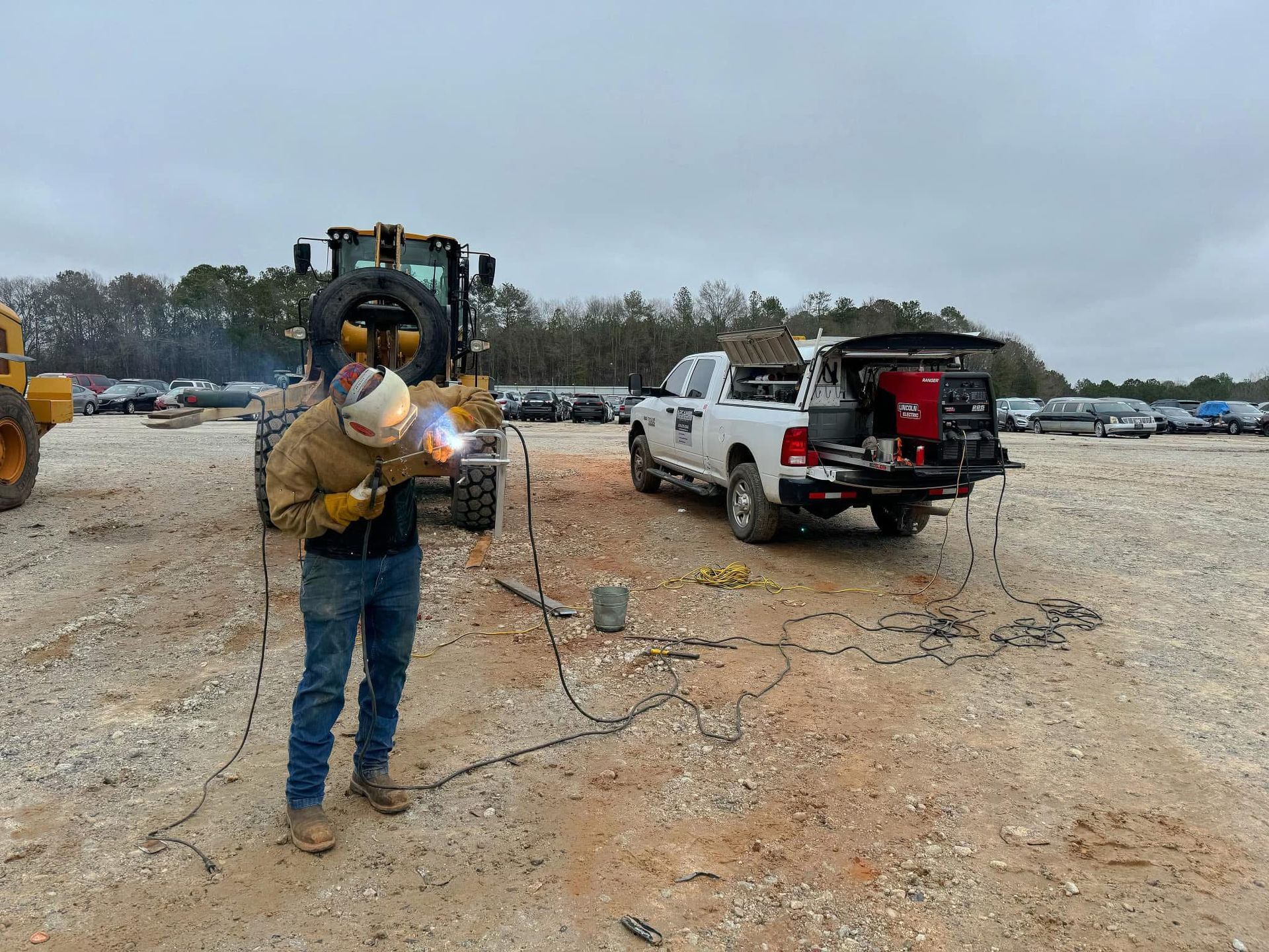 Welder wearing protective gear working on equipment outdoors next to a truck. Mobile welding services