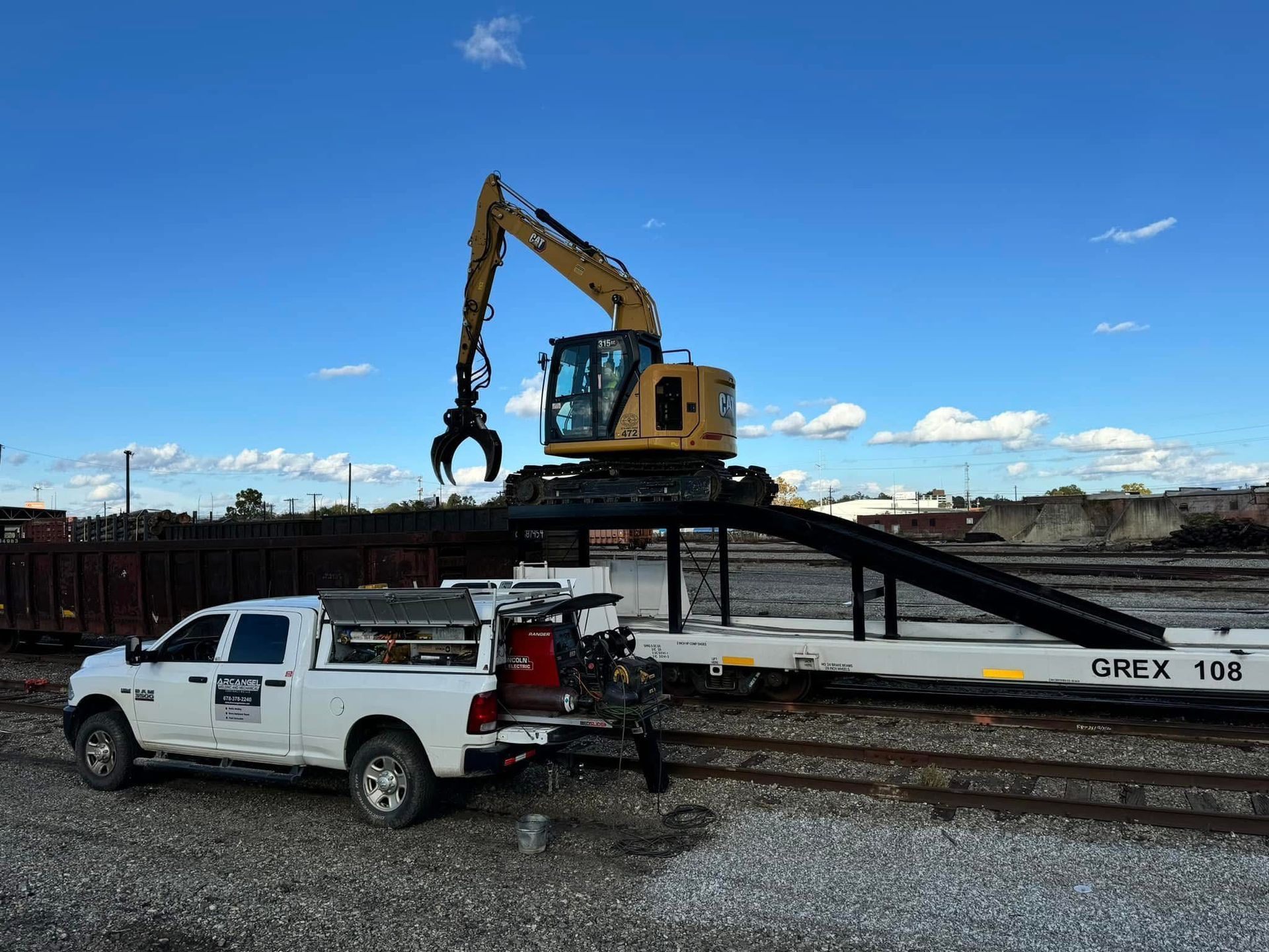 Excavator with grapple on flatbed rail car, truck with welder parked in a rail yard. Emergency mobile welding