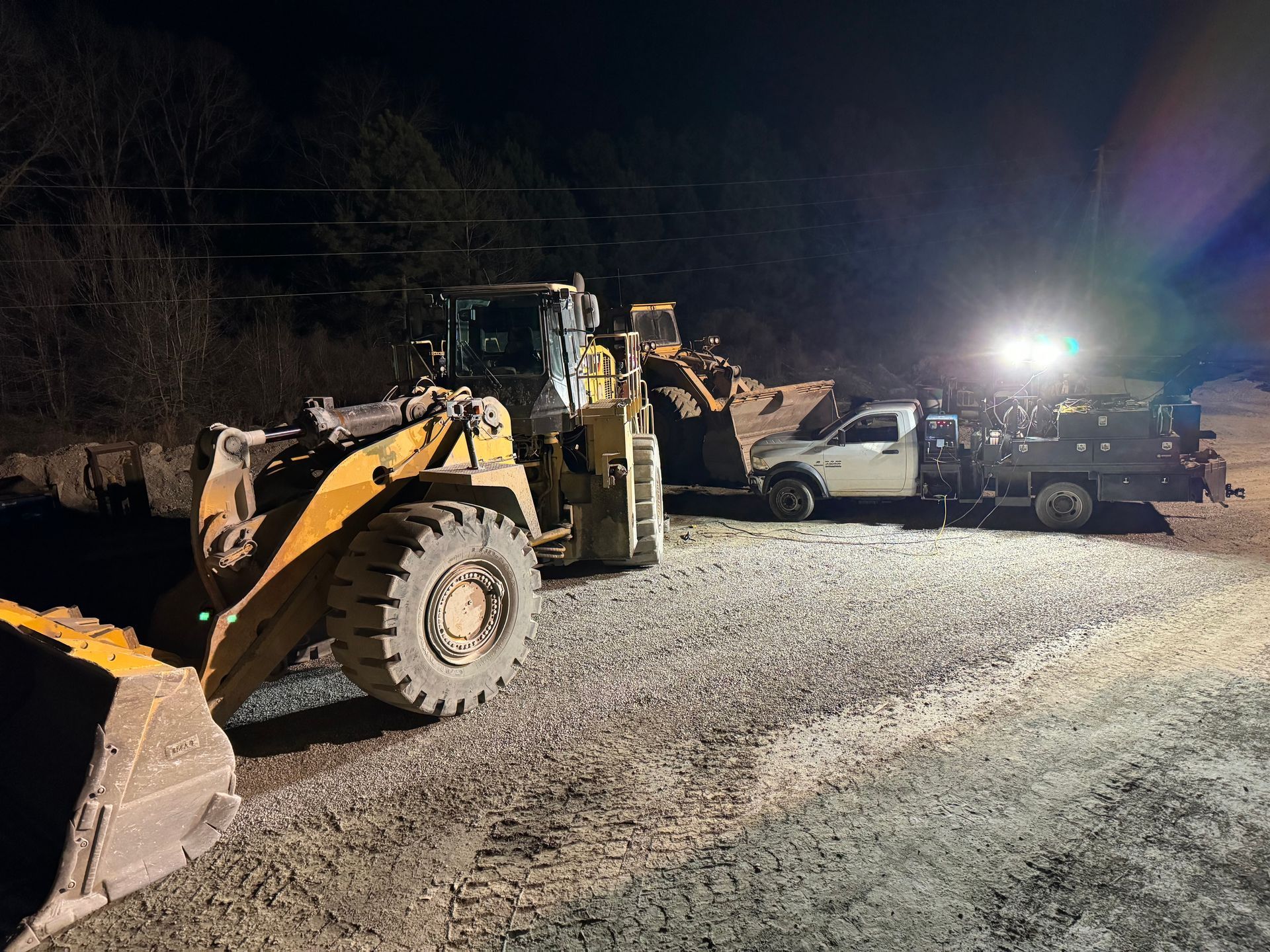 A front-end loader and a truck illuminated at night, likely construction equipment. Heavy Equipment Repair