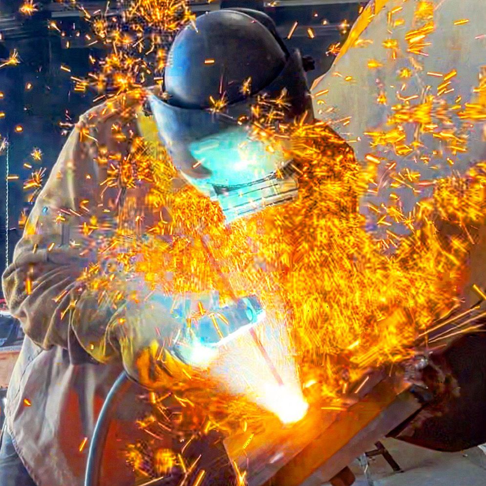 Welder in protective gear, sparks flying, welding metal in a workshop. Custom Parts Manufacturing
