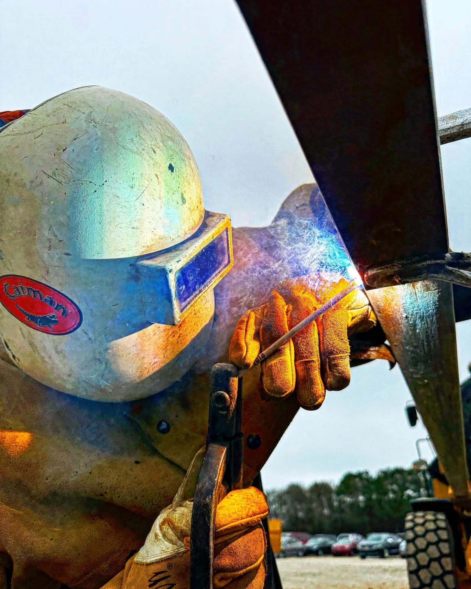 Welder wearing protective gear, welding metal outdoors. Field fabrication