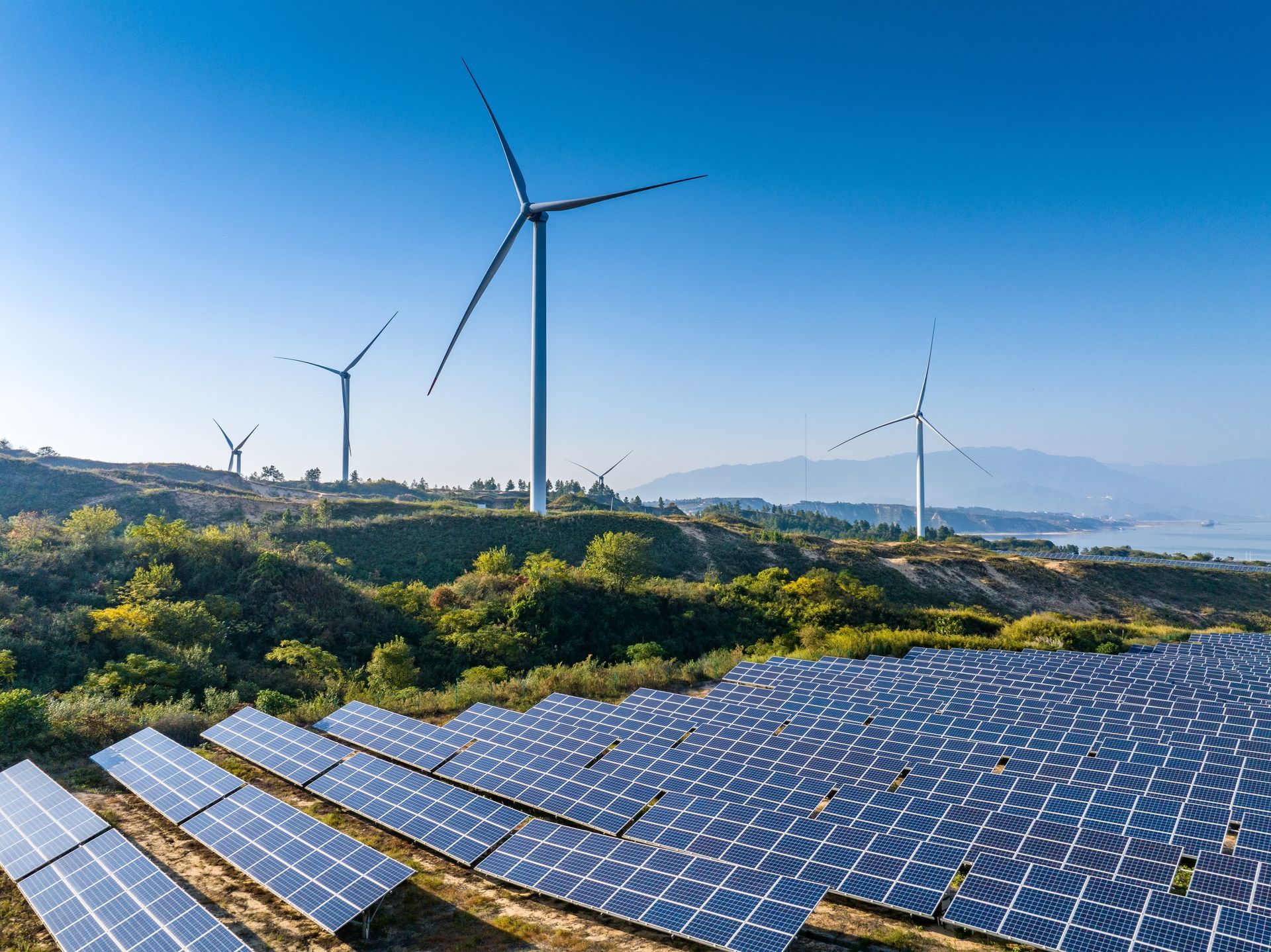 Wind turbines and solar panels generate power on a sunny hillside