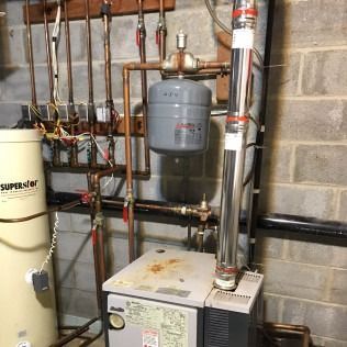 Heating system with pipes, tank, and a flue in a basement.