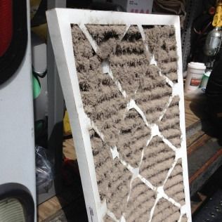 Dirty air filter, rectangular shape with white frame, heavily soiled with dust and debris.