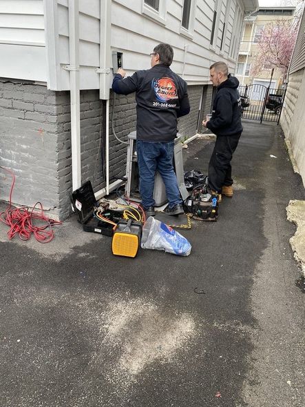 Two technicians working on electrical equipment outside a building.