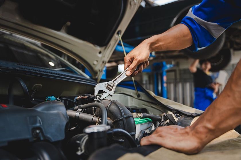 Mechanic using pliers to repair a car engine under the open hood in a garage