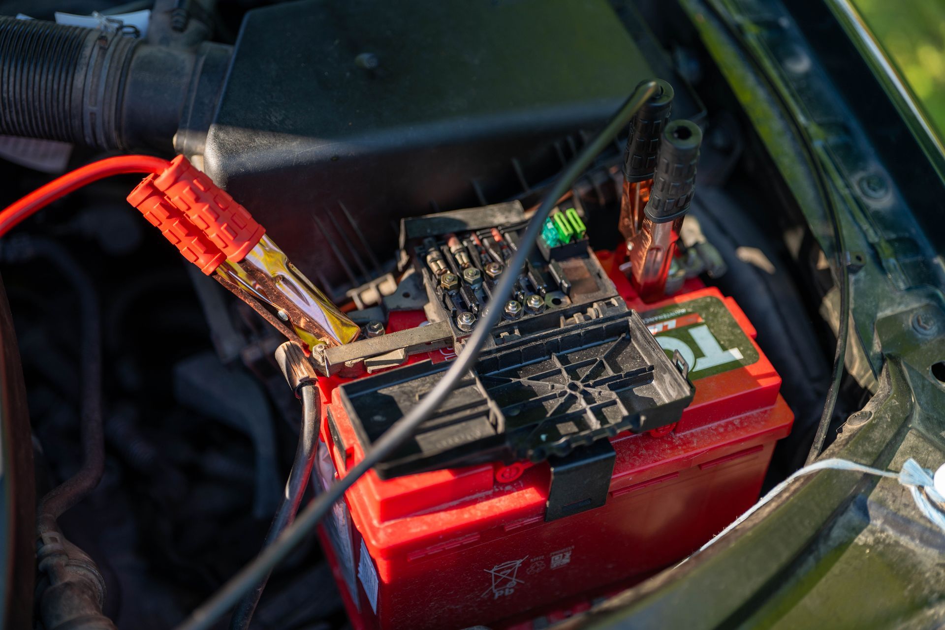 Small electronic circuit board with wires connected to a red battery pack inside a vehicle compartment