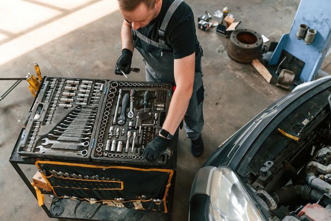 Mechanic leaning over an open toolbox beside a car in a garage