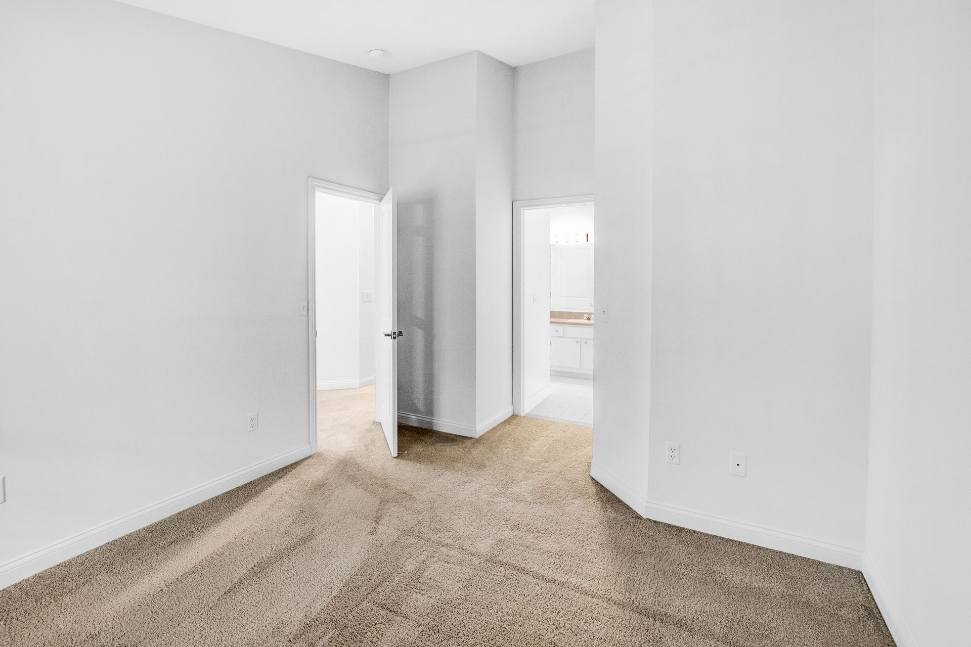 An empty bedroom with a brown carpet and white walls.