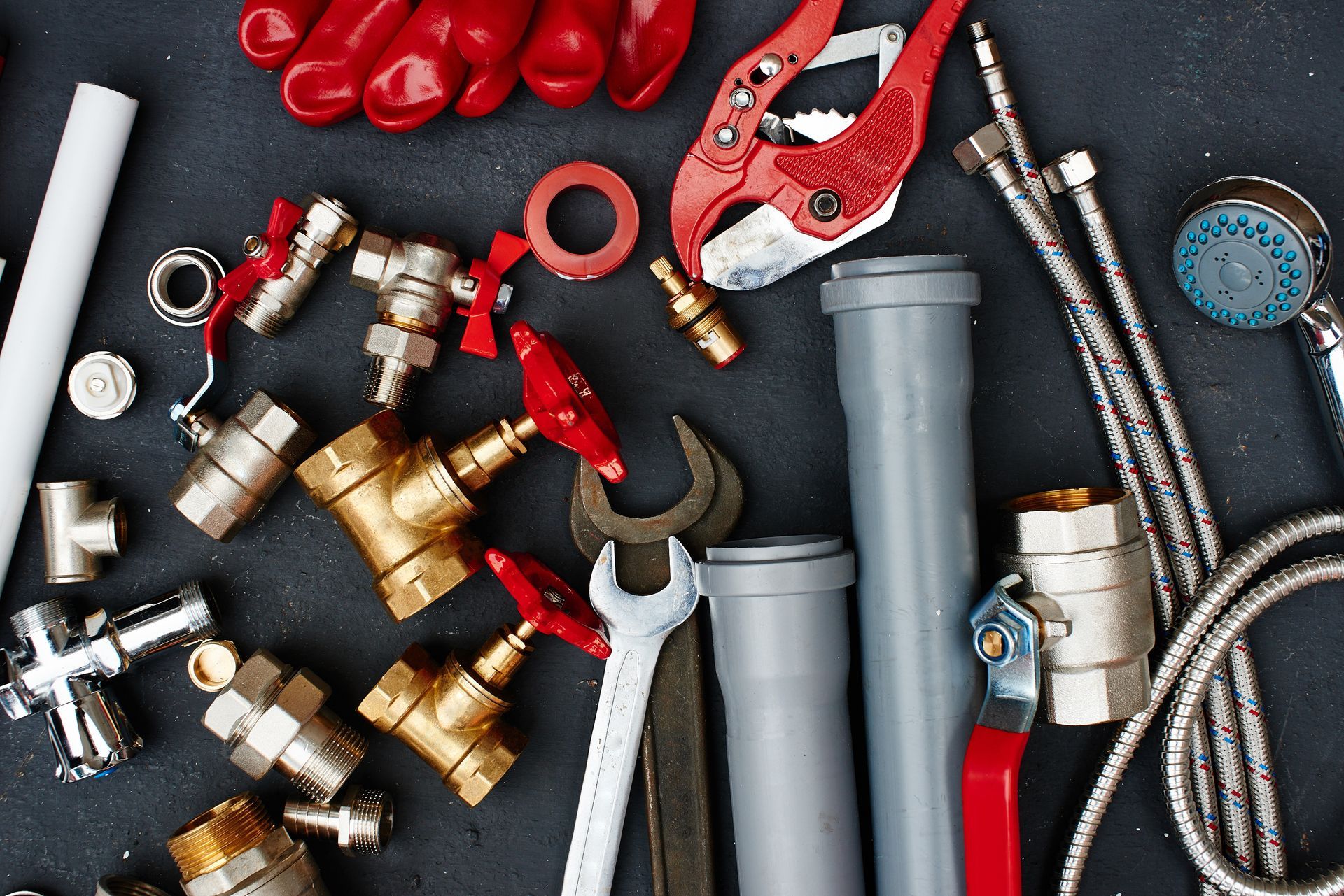 Assorted plumbing tools and fittings, including valves, pipes, wrenches, and pliers on a dark surface