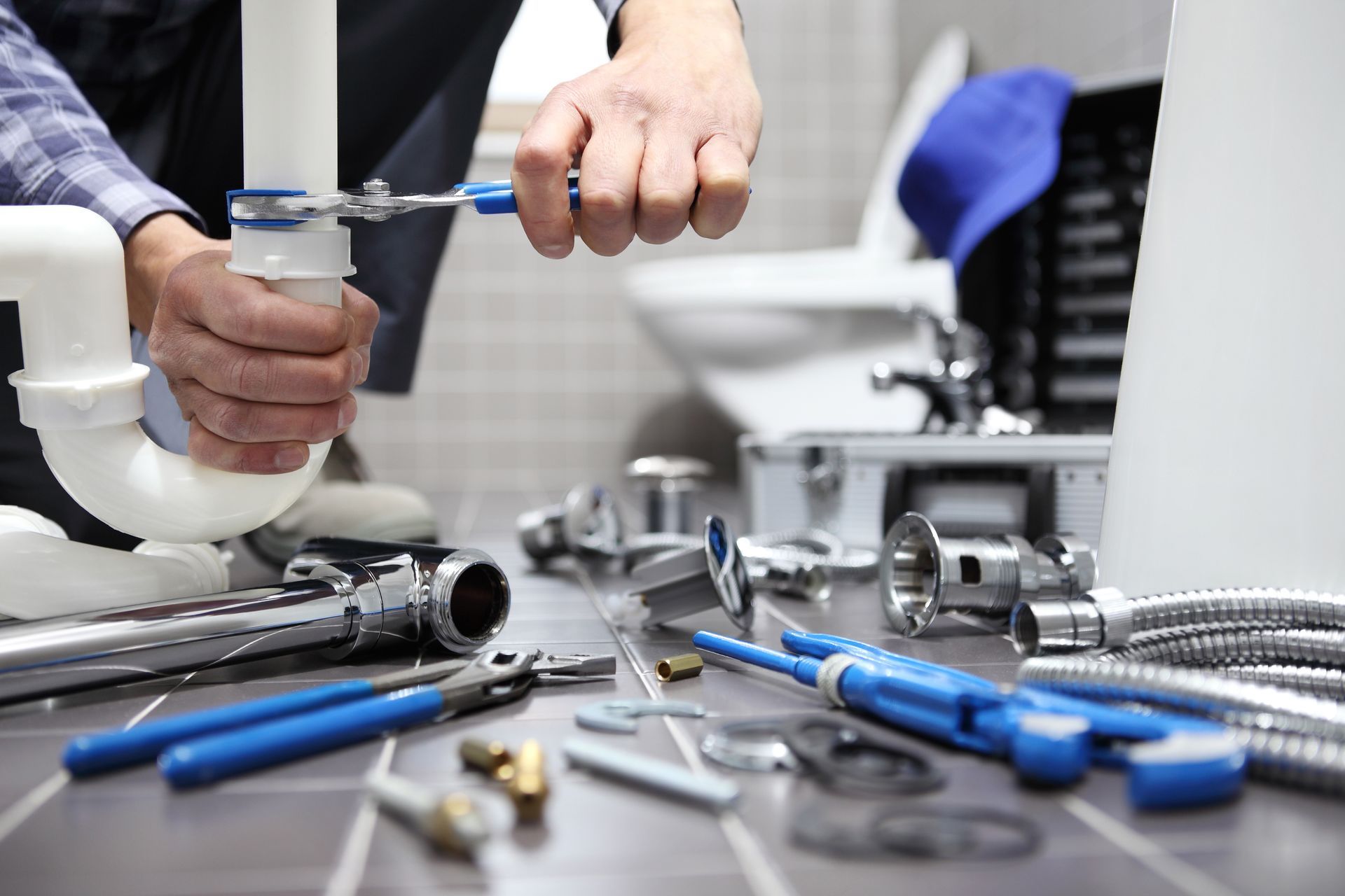 Hands assembling a plumbing fixture with blue-handled tools on a workbench