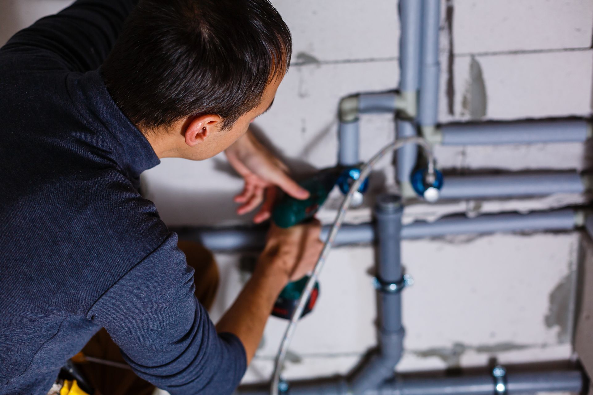 Person using a green power tool to work on exposed plumbing pipes in a wall