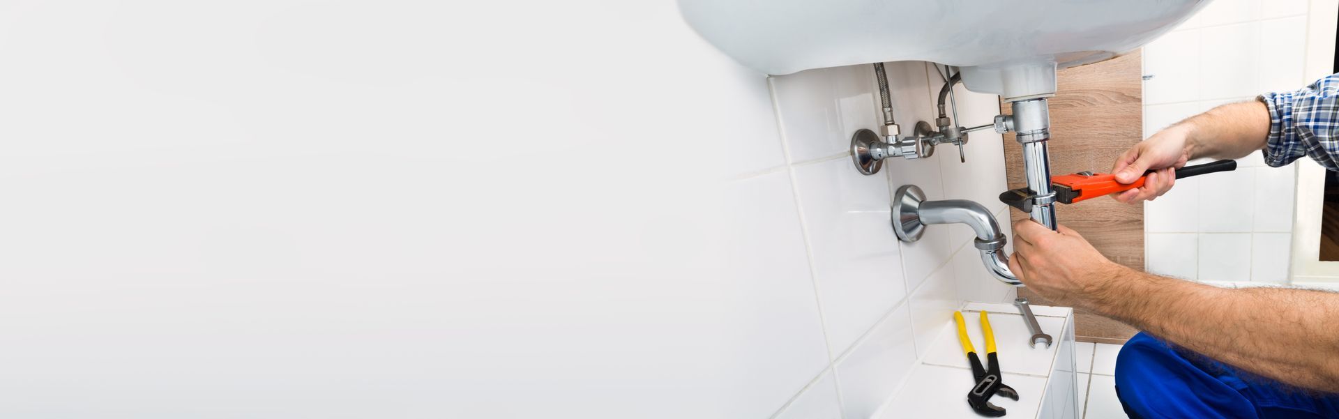 Plumber repairing a sink’s exposed pipes under a white bathroom wall