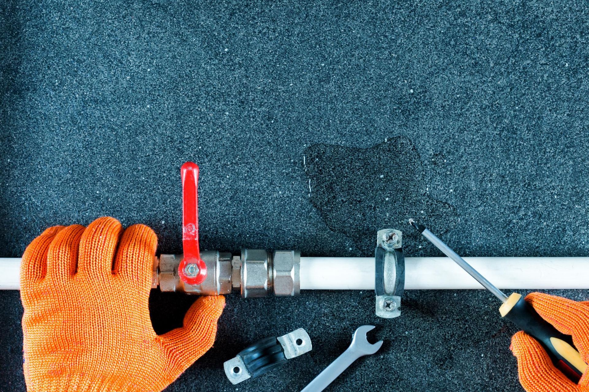 Hands In Orange Gloves Fixing Pipe With Tools Near Red Valve On Dark Surface — David Talbot Plumbing in Cranbrook, QLD
