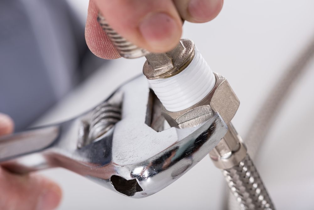 Hands Tightening Metal Fitting With Wrench Wrapped With White Tape — David Talbot Plumbing in Cranbrook, QLD