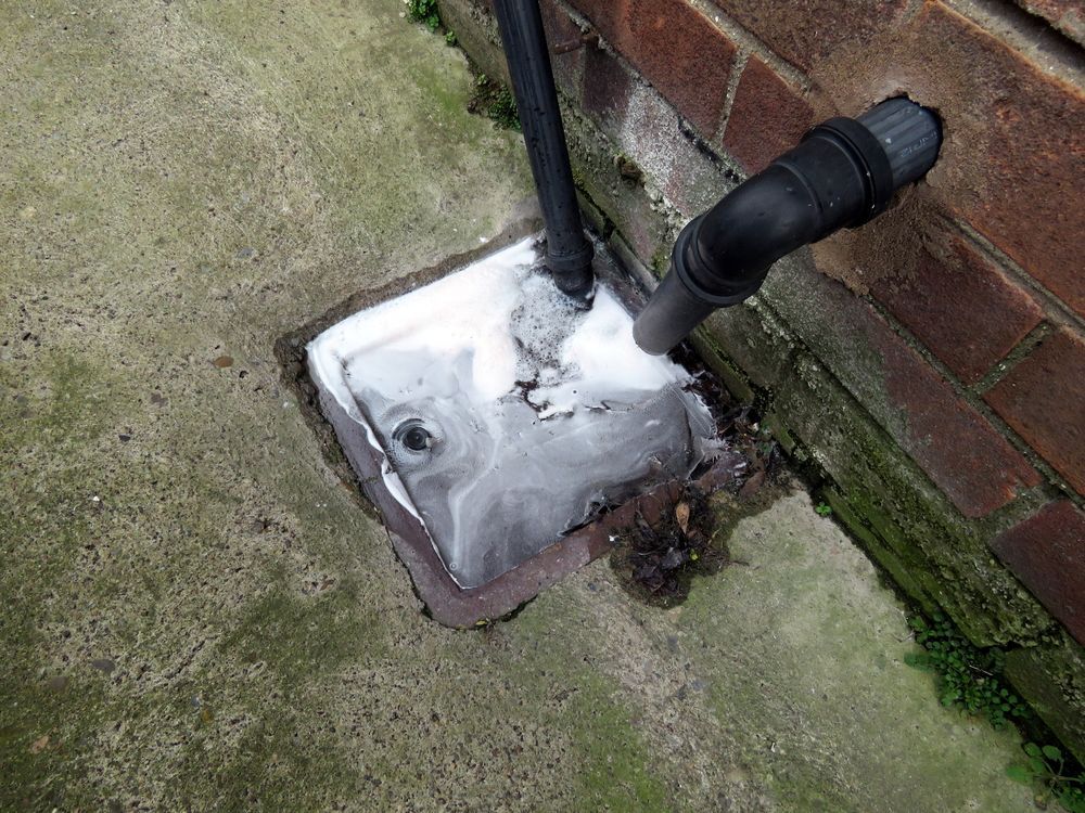 Concrete Patch With White Foam Around Two Black Pipes From Brick Wall — David Talbot Plumbing in Cranbrook, QLD