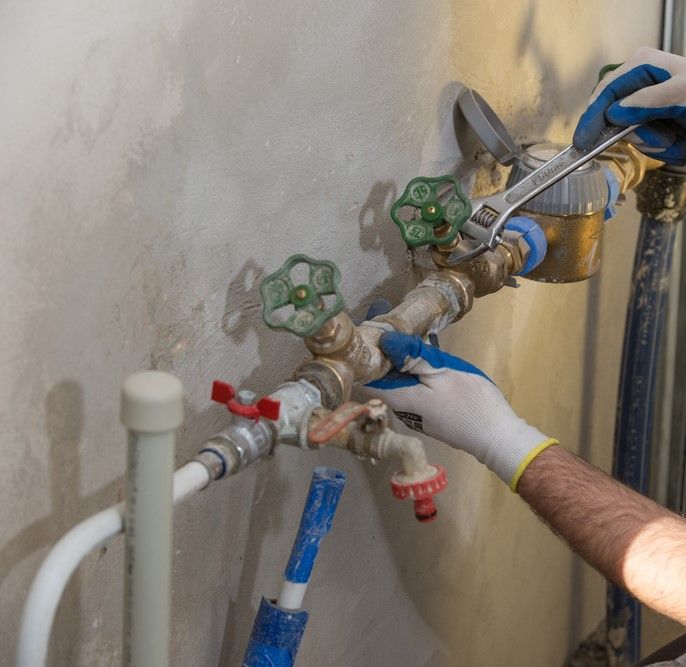 Plumber In Gloves Using Wrench On Water Pipes Near Wall — David Talbot Plumbing in Cranbrook, QLD