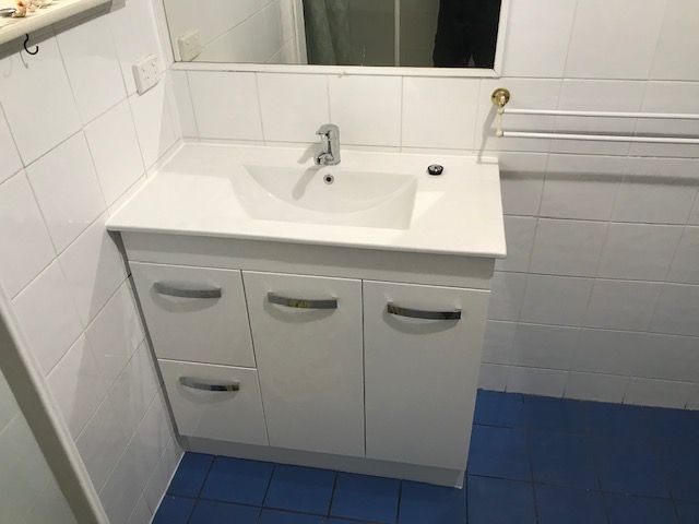 White Bathroom Vanity With Sink And Cabinet Doors On Blue Tiled Floor — David Talbot Plumbing in Cranbrook, QLD