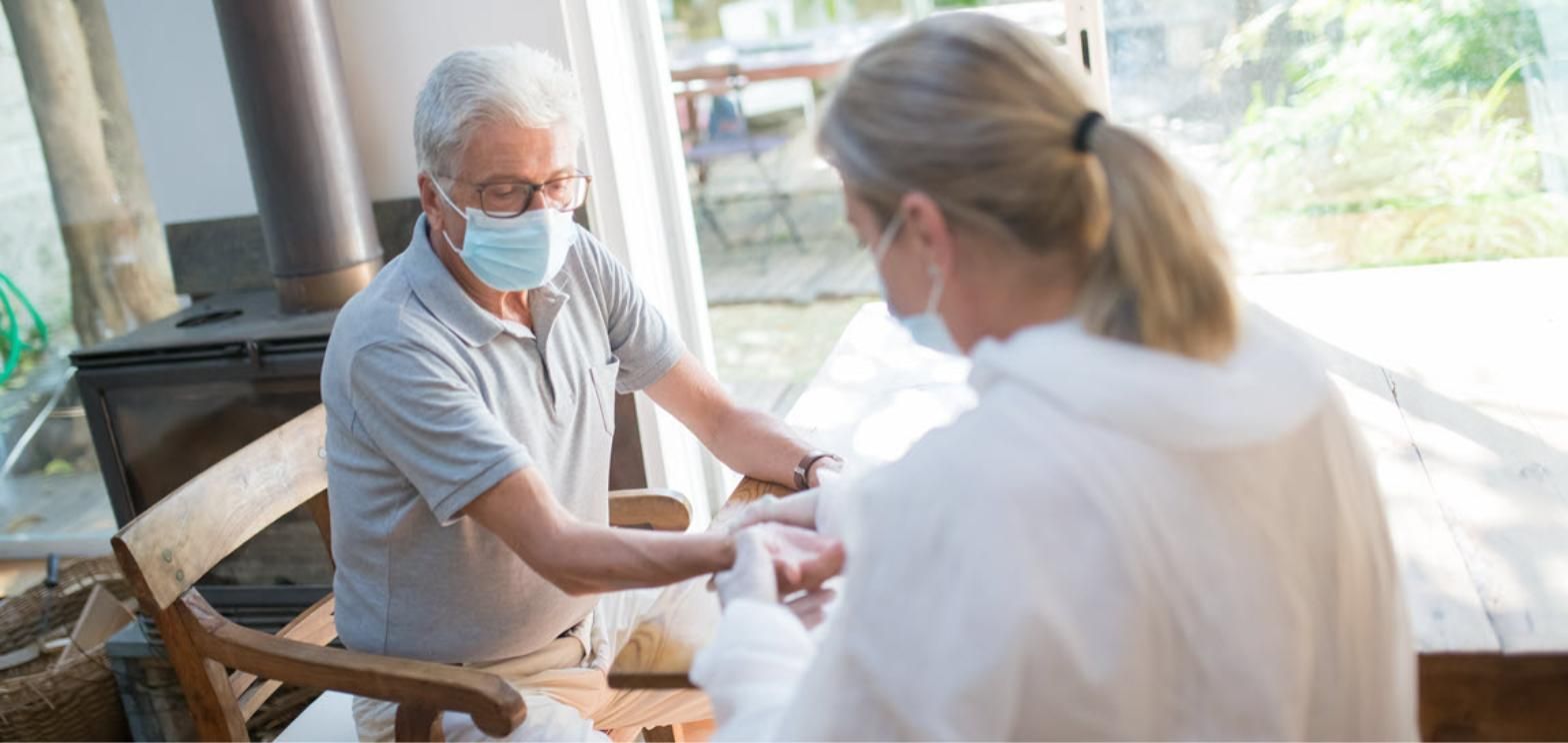 Masked older man receiving care from a masked healthcare worker at home