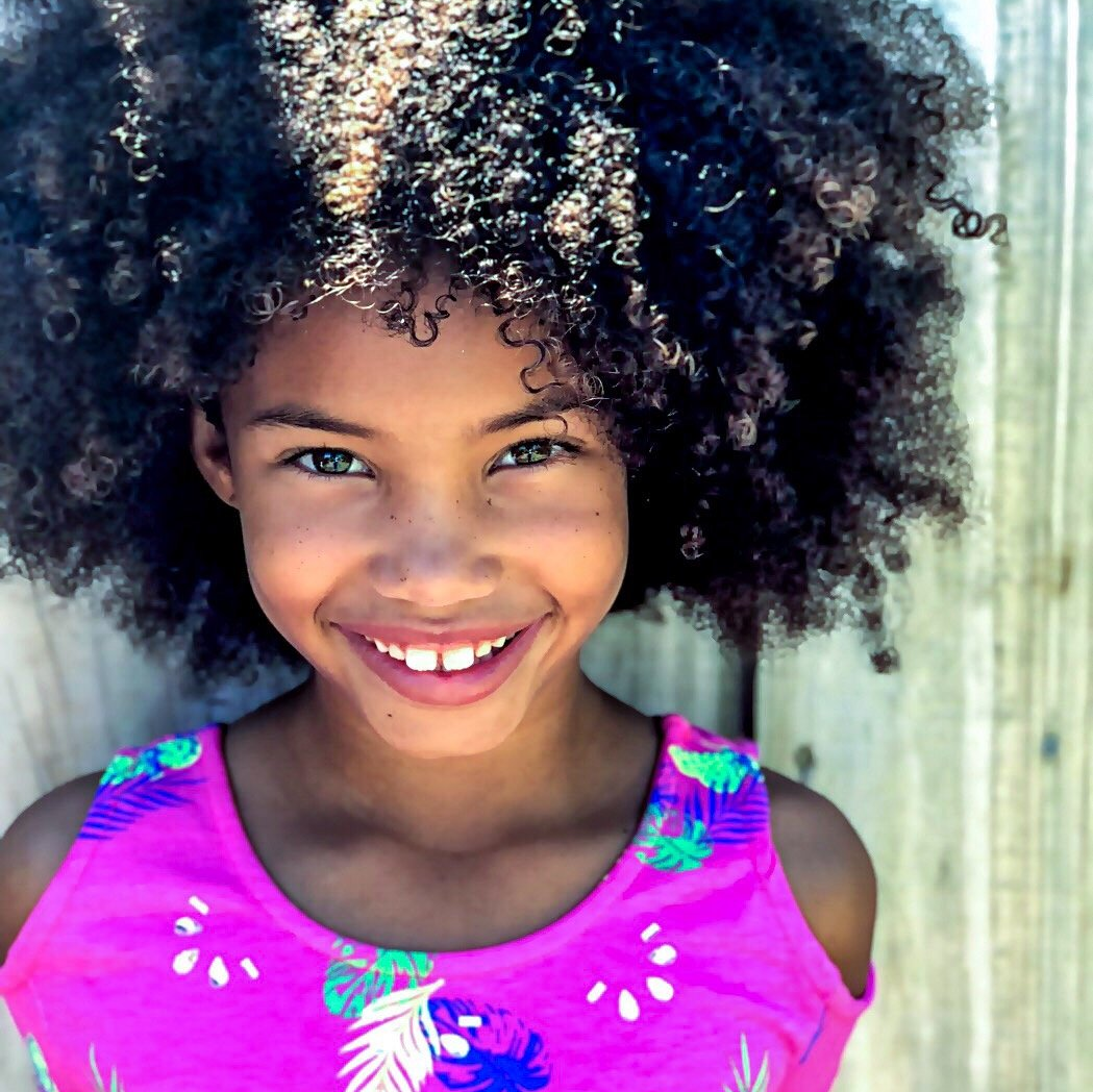 A young girl with curly hair is smiling for the camera
