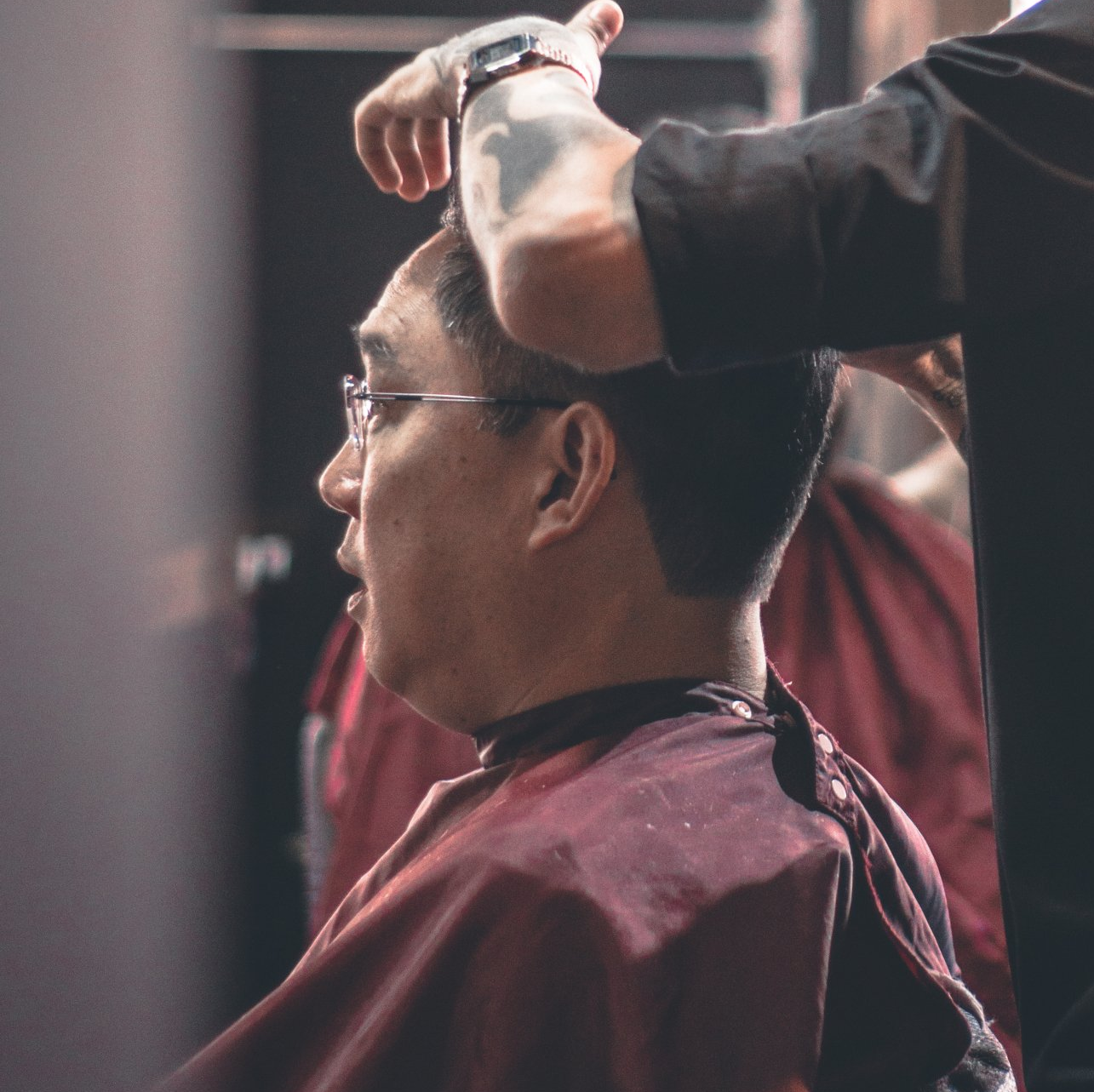 A man with glasses is getting his hair cut by a barber