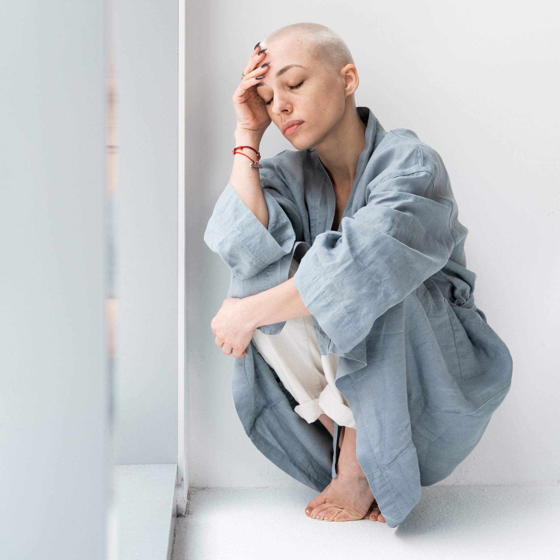 A woman with a bald head is kneeling down in front of a window.