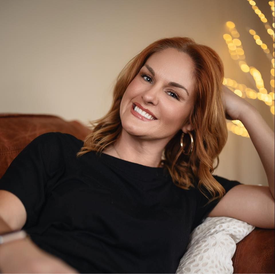 A woman in a black shirt is smiling while sitting on a couch