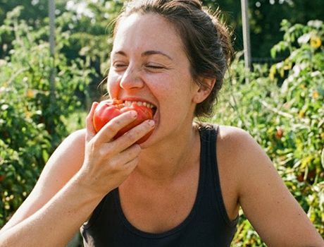 Een vrouw neemt een hap van een rijpe rode tomaat in een moestuin, met gesloten ogen, en geniet van de heerlijke smaak.