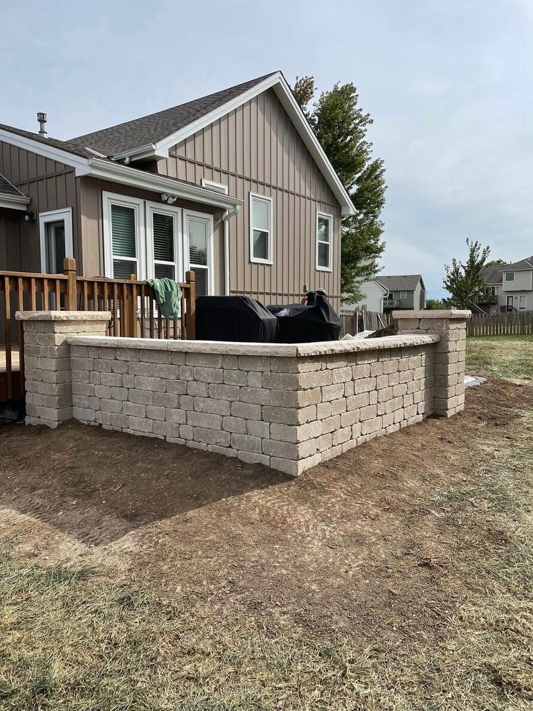 Back patio with tan brick raised planter, outdoor seating, and a beige house in the background