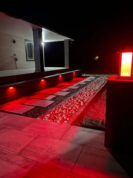 Red-lit patio walkway beside a house at night, with a glowing lamp on the right.