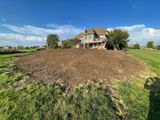 Rural house behind a large freshly tilled dirt mound under a blue sky with clouds