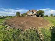 Rural house behind a large freshly tilled dirt mound under a blue sky with clouds