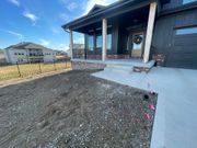 New house front porch with concrete walkway and unfinished dirt yard under a blue sky