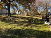 Leaf-covered backyard with trees, sunlight, and a small patio area beside a house