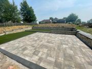Stone patio with retaining walls and a strip of grass in a landscaped backyard