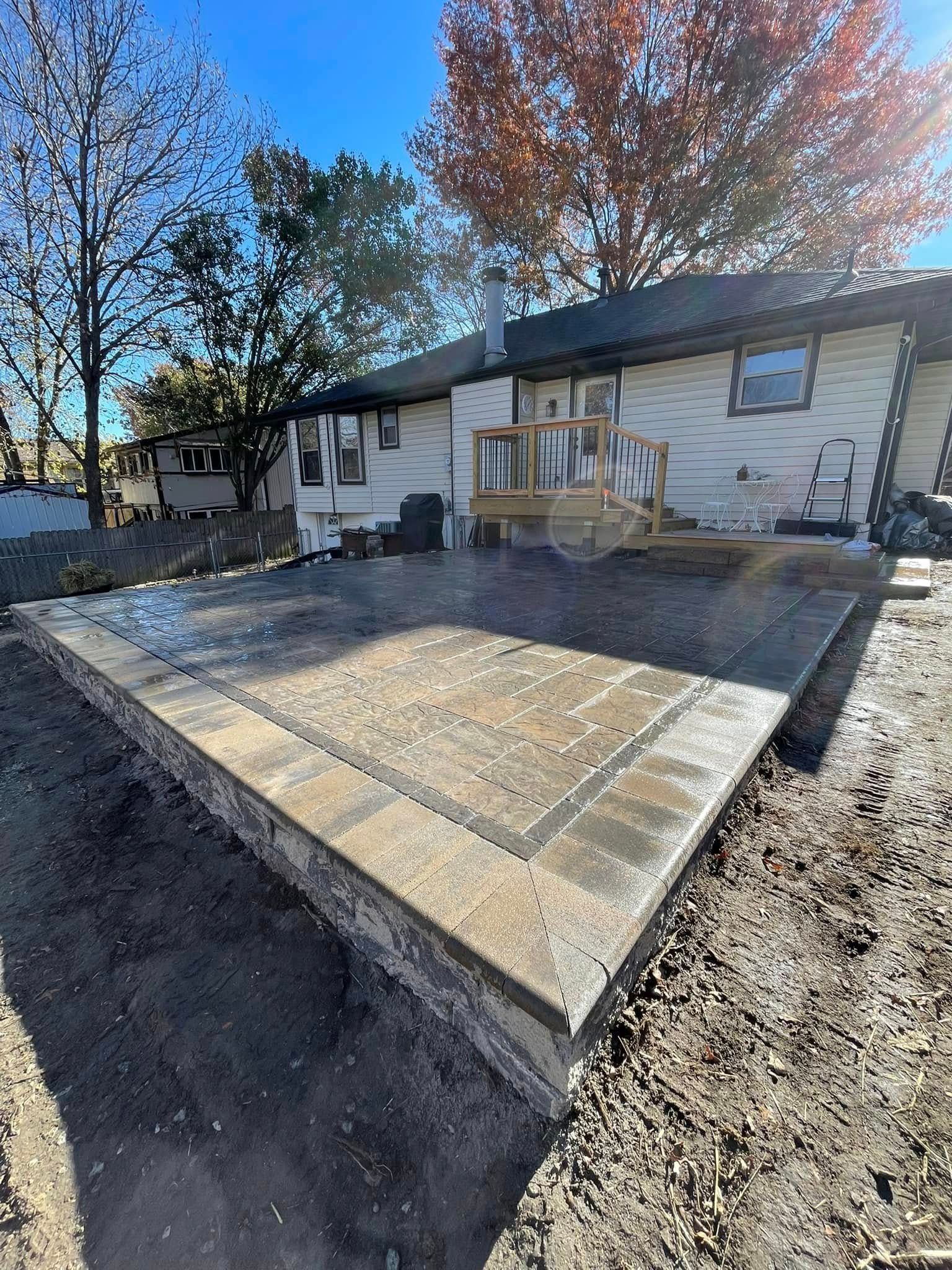 Concrete patio ramp leading to a house deck in a backyard, with autumn trees and gravel around it