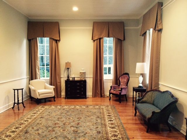 Elegant living room with hardwood floors, large rug, tall windows, and assorted chairs and lamps.