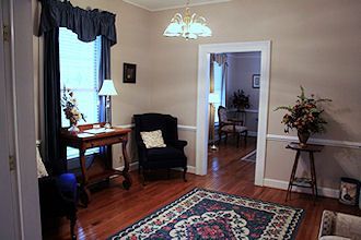 Cozy living room with a rug, armchair, table lamp, and open doorway to a dining room.