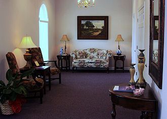 Cozy living room with floral sofa, lamps, wall art, and small tables under soft lighting