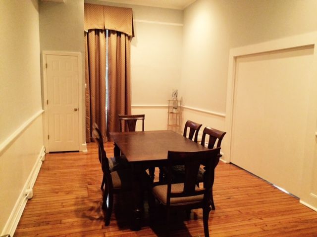 Dining room with a dark wood table and chairs on a hardwood floor, cream walls, and a curtained doorway.