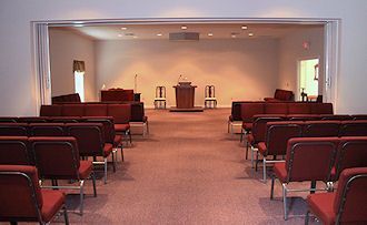 Empty chapel with rows of red chairs facing a podium and lectern at the front.