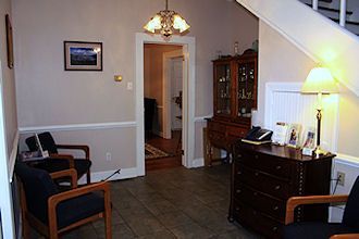 Small living room with chairs, a wooden cabinet, lamp, and an open doorway to a hallway.