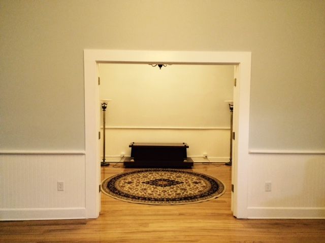 Empty doorway opening into a small room with a black bench and oval rug on wood flooring