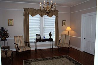 Elegant living room with striped armchairs, chandelier, desk by window, and warm lamp lighting