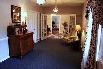 Empty living room with dark carpet, French doors, wooden cabinet, lamps, and floral curtains