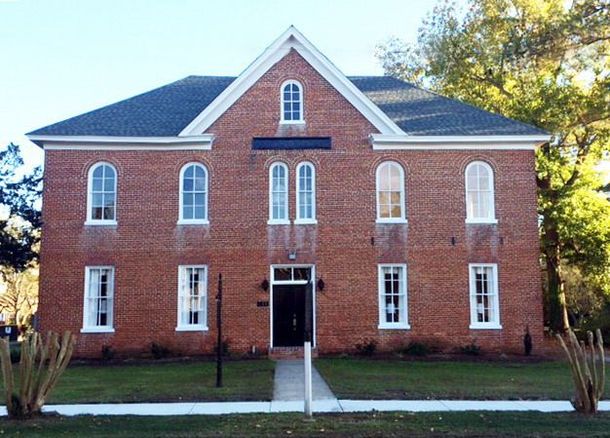 Red brick building with white trim and a central entrance, framed by trees and lawn.