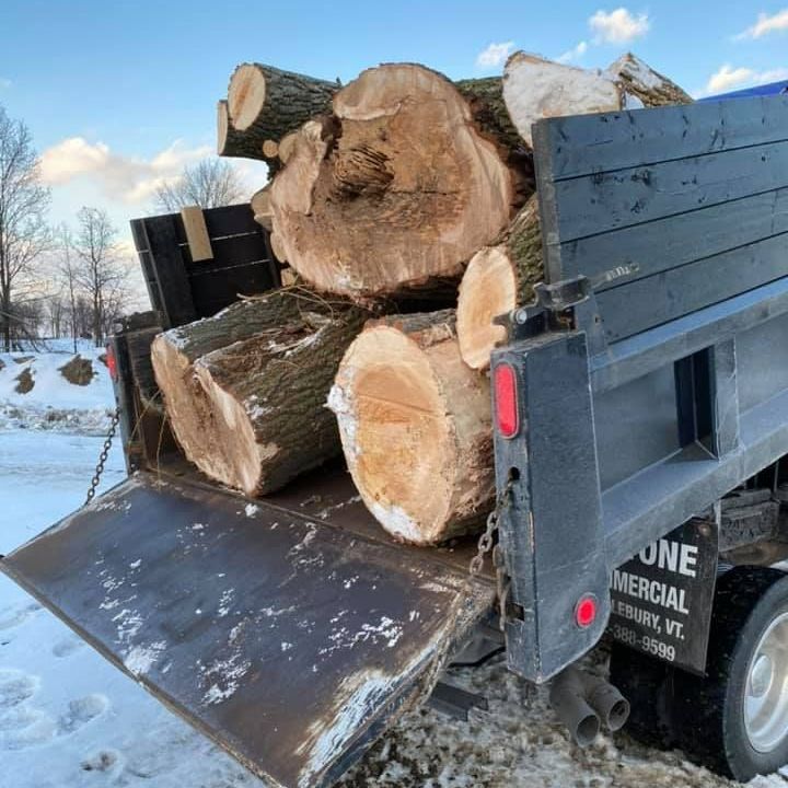 Logs fill a truck bed, the ramp open, resting in snow; Vermont.