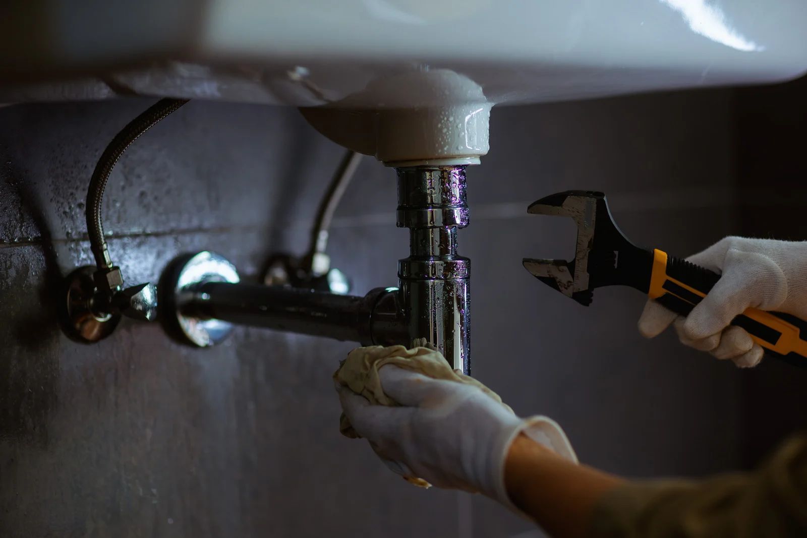 Plumber fixing a leaky sink; they are using a wrench and a cloth.